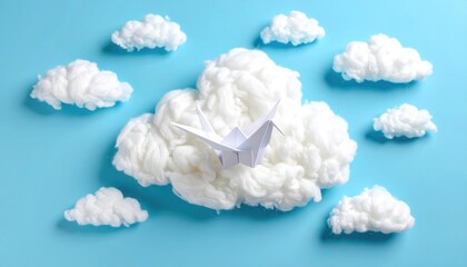 Origami crane rests on a fluffy cloud-like material amidst small puffy clouds, all on a soft blue background creating a dreamy, peaceful ambiance