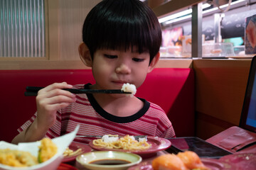 appy Asian boy enjoying fresh sushi at a Japanese restaurant with chopsticks and a big smile