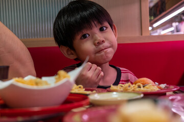 Asian child eating sushi with chopsticks at restaurant table, enjoying traditional Japanese food