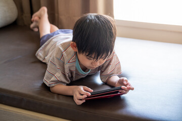 Asian boy lying on bed happily playing with mobile phone in cozy bedroom leisure time scene