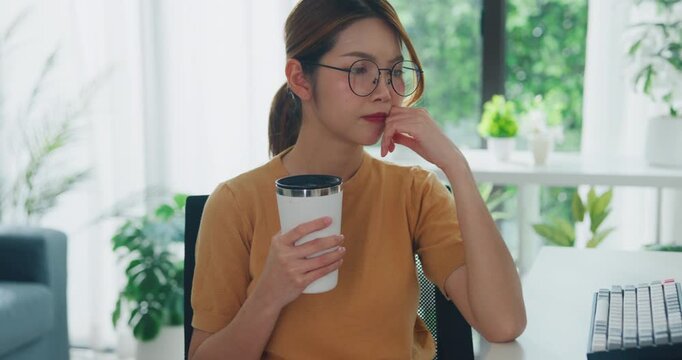 Young Asia female freelance eyeglasses drink coffee and type write prompt AI bot IT app program nomad, video game, terminal with coding, user interface, data center on desktop computer at home office.