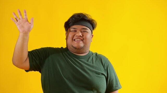 Friendly overweight man greeting with a hello gesture isolated on a yellow background