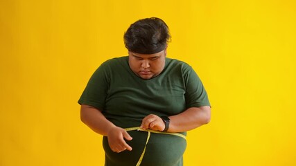Overweight man measuring waist circumference after exercising isolated on yellow background