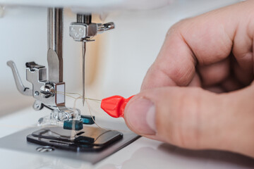 Male dressmaker putting thread in sewing machine, closeup photo. Incorrect threading of sewing machine needle from wrong side, close-up mistake example