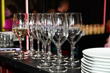 Empty wine glasses neatly arranged on a bar counter with a stack of plates, prepared for a night party and festive celebration atmosphere.