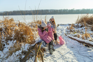 Mother and daughters have a picnic on the shore of the lake in the winter. Children drinking hot tea