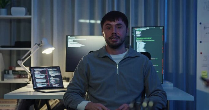 Adult male freelance programmer work late speak in online meeting video conference and looking at camera in tech office night. Artificial intelligence, robotics, user interface, machine learning.