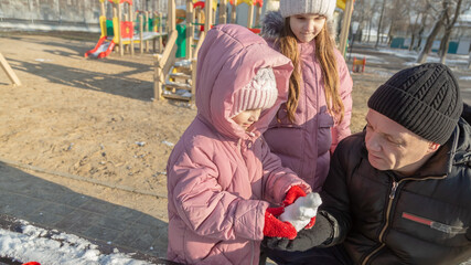 Grandfather playing with her granddaughters on the playground in the park in winter