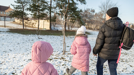 Grandfather walks with his granddaughters after school in the park in sunny winter day
