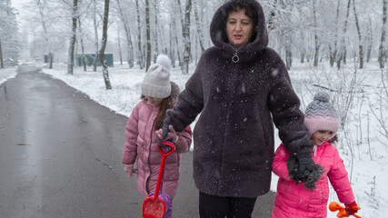 Grandmother with grandchildren in warm clothes playing outdoors in winter park, enjoying snowy...