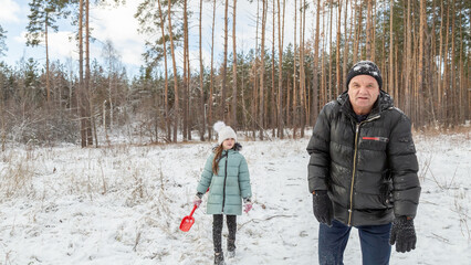 Little girls play with snow with her grandfather in winter forest