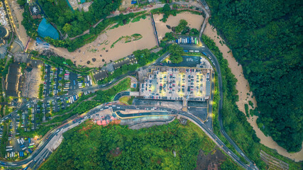 Aerial top-down drone view of an illuminated parking lot and highway next to a muddy river at night.