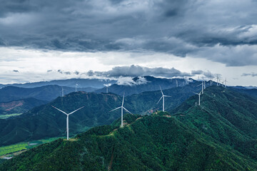 Panoramic landscape of a large wind farm on green mountain tops under cloudy sky.