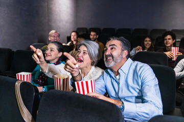 Groups of people enjoying a movie in the cinema, pointing at the screen while sharing popcorn and experiencing the excitement together