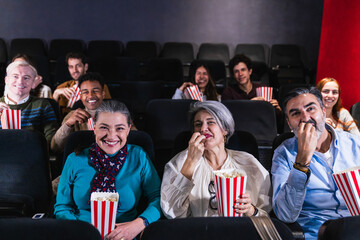 Multi ethnic group of cheerful people laughing and eating popcorn while watching a movie at the cinema