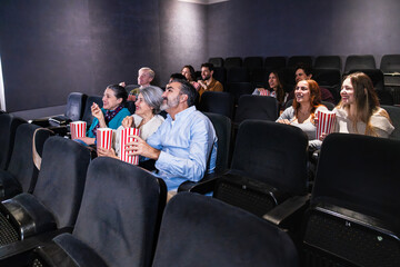 Group of people watching a movie and eating popcorn, enjoying their leisure time at the cinema