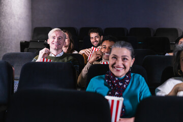 Group of cheerful multi ethnic friends enjoying film screening and eating popcorn, having fun together at the movie theater