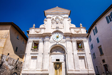 White facade of Palazzo Comunale with its clock and fountain under a clear blue sky during a sunny summer day in Spoleto, Umbria, central Italy