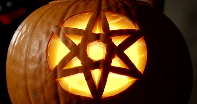 A jack-o'-lantern carved with a glowing hexagram symbol for Halloween.