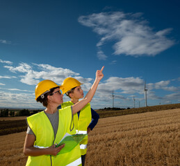 Professional female engineer wearing safety gear demonstrating wind turbine operations, pointing...