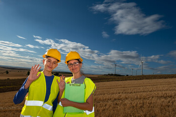 Renewable energy professional training student near wind turbines, wearing safety gear, waving and...