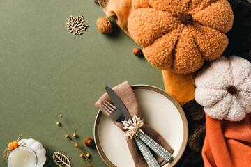 Cozy autumn table setting with plush pumpkins, cutlery in rustic napkin on plate, and festive decor