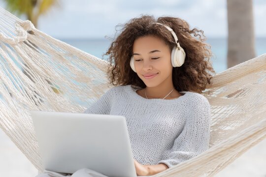 Young african female relaxing in hammock with laptop and headphones outdoors
