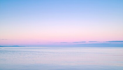 A tranquil seascape displays a smooth ocean reflecting a gradient sky of soft blue and pink hues at sunrise or sunset, creating a serene atmosphere
