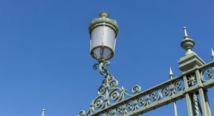 Vintage ornate street lamp with wrought iron fence against clear blue sky