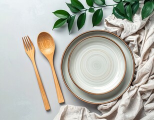 A natural, pastel background with plates, wooden cutlery, a linen cloth, and a green sprig. Table setting, tableware