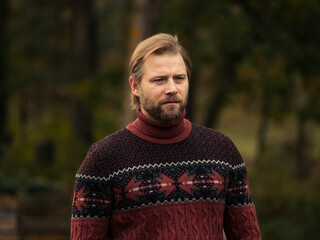 Portrait of handsome young man in wool knitted sweater outdoors. Male with long hair and beard feel...
