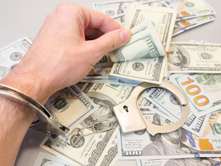 Folded hands and handcuffed hands resting on a table in front of money.