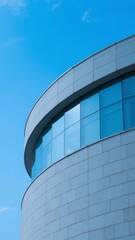 Obraz premium Curved Modern Building with Glass Windows Against a Clear Blue Sky