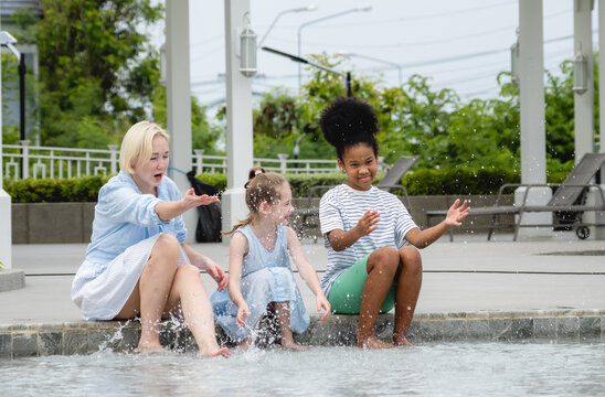Mother two children joyfully run through shallow pool while holding hand. scene set in modern outdoor recreational area with architectural elements like capturing lively and carefree summer moment.