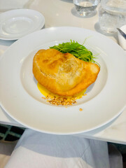 Stuffed pastry pouch served on a plate with fresh arugula and chopped pistachios