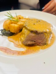 Juicy beef fillet served with a side of golden roasted potatoes. A delicious gourmet meat dish presented on a white plate, perfect for illustrating fine dining, traditional European cuisine