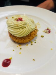 Elegant choux pastry filled with pistachio cream, artfully presented on a white plate with raspberry coulis dots and pistachio crumbles.