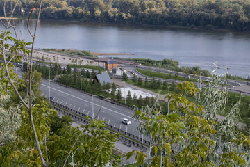 Automobile road with a car and embankment with walking areas along the river. Trees. Aerial view....