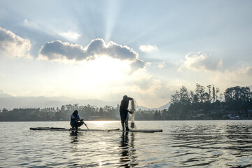 Two Men On A Bamboo Raft, Against A Beautiful Sunlit Lake, Prepare Their Fishing Net