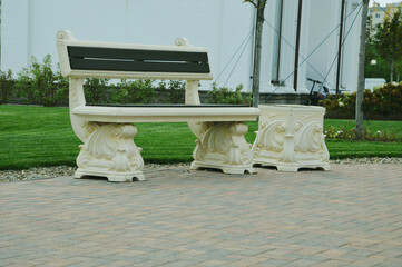 White carved stone bench and urn with spiral elements in the city park. The seat has wooden brown...