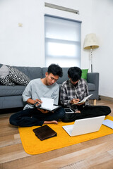 Two Students Work Together At Home Using Laptop While Writes In Notebook On The Living Room Floor