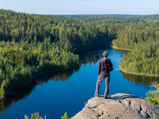 A man stands on a rock near a forest lake on a beautiful summer day.