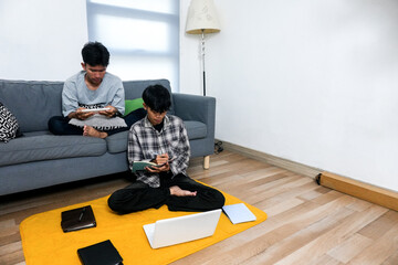 Student Works On Laptop On The Floor While Friend Using Digital Tablet On The Couch