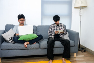 Two Young Asian Men Sitting On Couch Working Together With Laptop And Book