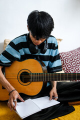 Young Asian Male Musician Wearing Headphones Around Neck Enjoys Moment Of Learning Guitar Notes