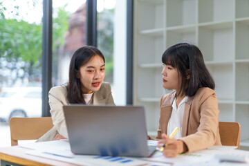 Two asian businesswomen having a business meeting, analyzing financial charts using laptop computer in the office