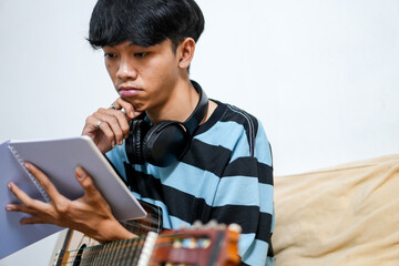 Serious Male Artist With Headphones And Guitar Looks At Songbook Contemplating Next Musical Idea