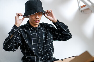 Focused Young Asian Man Adjusts Stylish Black Bucket Hat