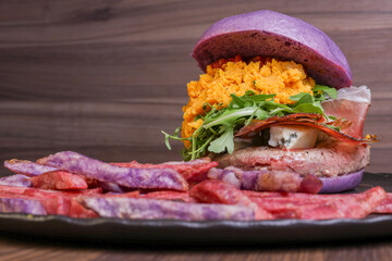 Panino da pub viola ripieno di hamburger, pancetta, rucola, zucca e mozzarella servito in un pub con contorno di patate viola