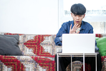 Young Asian Man As Freelancer Greetings With Waving Hand On Laptop During Video Call